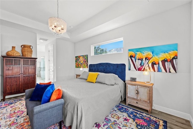 bedroom featuring wood-type flooring, connected bathroom, a tray ceiling, and a notable chandelier