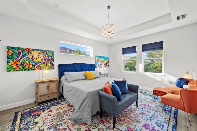 bedroom featuring a raised ceiling, a chandelier, and light hardwood / wood-style floors