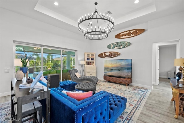 living room with a chandelier, light wood-type flooring, and a tray ceiling