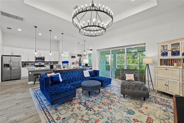 living room with plenty of natural light, light hardwood / wood-style floors, a high ceiling, and a chandelier