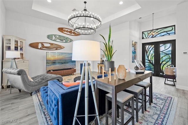 dining area featuring an inviting chandelier, french doors, light hardwood / wood-style flooring, and a tray ceiling