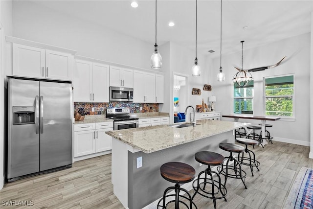 kitchen with white cabinets, stainless steel appliances, a center island with sink, and sink