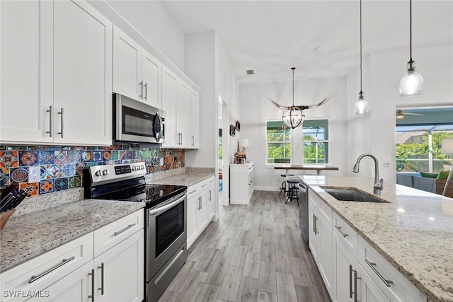 kitchen with white cabinets, sink, hanging light fixtures, appliances with stainless steel finishes, and light stone counters