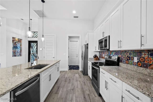 kitchen with white cabinets, sink, hanging light fixtures, light stone countertops, and stainless steel appliances