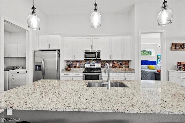 kitchen with stainless steel appliances, sink, pendant lighting, white cabinets, and washing machine and dryer