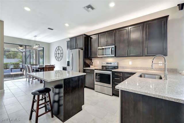 kitchen with sink, stainless steel appliances, light stone counters, decorative light fixtures, and a kitchen bar