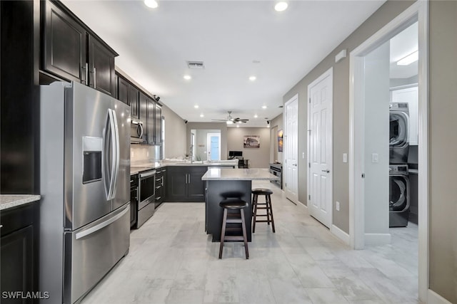 kitchen featuring ceiling fan, light stone countertops, stainless steel appliances, a kitchen breakfast bar, and a kitchen island