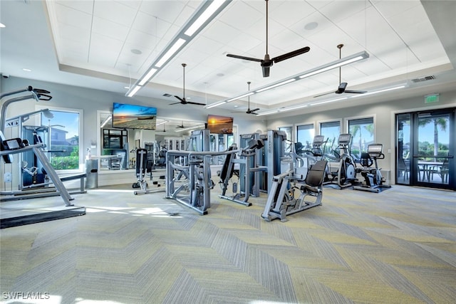 exercise room featuring light carpet, a tray ceiling, and ceiling fan