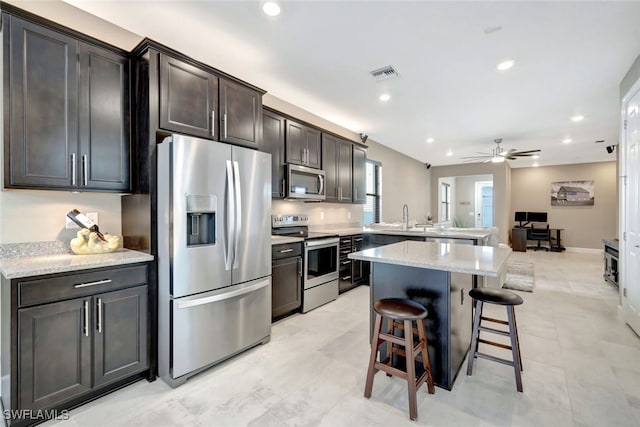 kitchen featuring light stone countertops, a breakfast bar, stainless steel appliances, ceiling fan, and a kitchen island