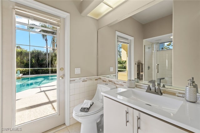 bathroom featuring a wealth of natural light, tile patterned flooring, toilet, vanity, and tile walls