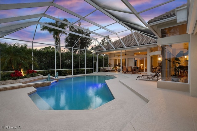 pool at dusk with glass enclosure, ceiling fan, a patio, and an in ground hot tub