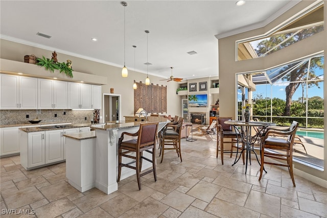 kitchen featuring light stone countertops, ceiling fan, decorative light fixtures, white cabinetry, and an island with sink