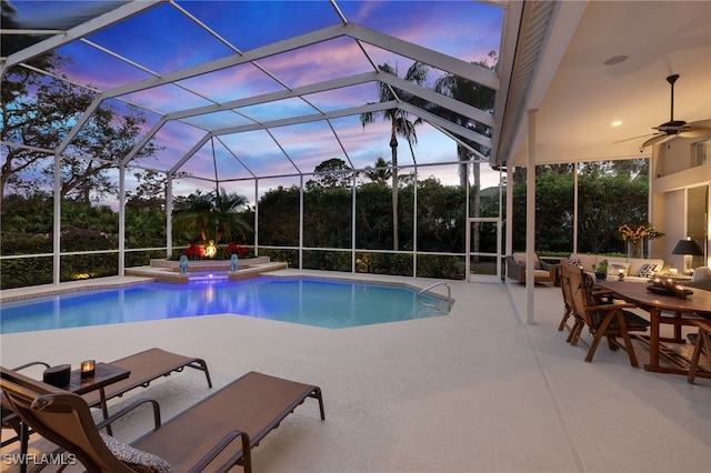 pool at dusk featuring glass enclosure, a patio area, and an in ground hot tub