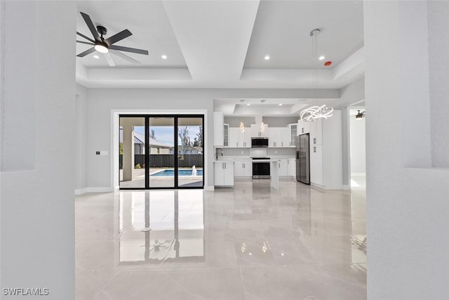 unfurnished living room with ceiling fan, a tray ceiling, a sink, and baseboards