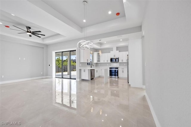 living room with ceiling fan with notable chandelier, a tray ceiling, recessed lighting, and baseboards