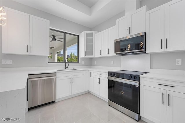 kitchen with glass insert cabinets, appliances with stainless steel finishes, light countertops, white cabinetry, and a sink