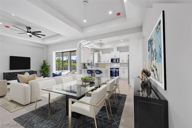 dining area featuring ceiling fan with notable chandelier, a raised ceiling, and sink