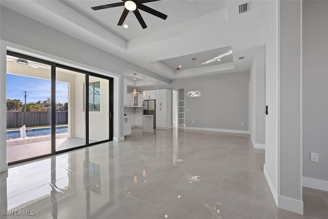 unfurnished living room with ceiling fan, a tray ceiling, visible vents, and baseboards