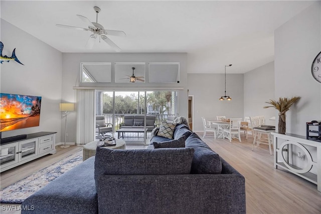 living room featuring ceiling fan, a towering ceiling, and light hardwood / wood-style flooring