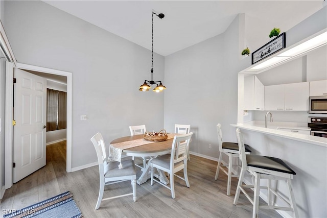 dining area featuring high vaulted ceiling, an inviting chandelier, light hardwood / wood-style flooring, and sink