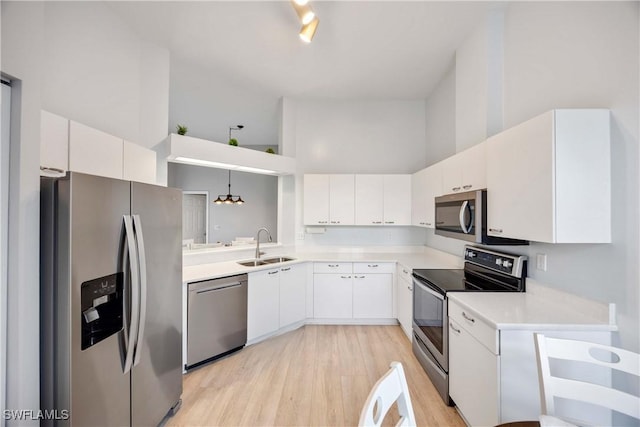 kitchen featuring stainless steel appliances, sink, decorative light fixtures, a high ceiling, and white cabinetry