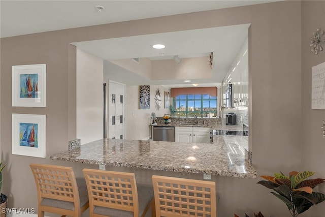 kitchen featuring light stone countertops, white cabinetry, a kitchen bar, and stainless steel dishwasher