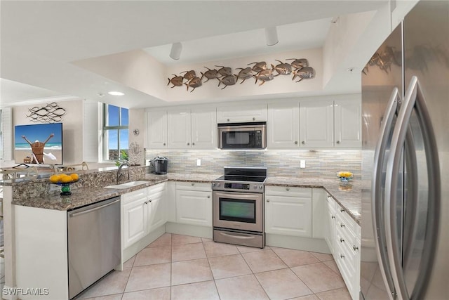 kitchen with kitchen peninsula, light stone countertops, stainless steel appliances, sink, and white cabinets