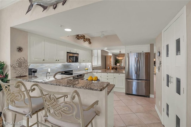 kitchen featuring kitchen peninsula, dark stone countertops, decorative light fixtures, white cabinets, and appliances with stainless steel finishes