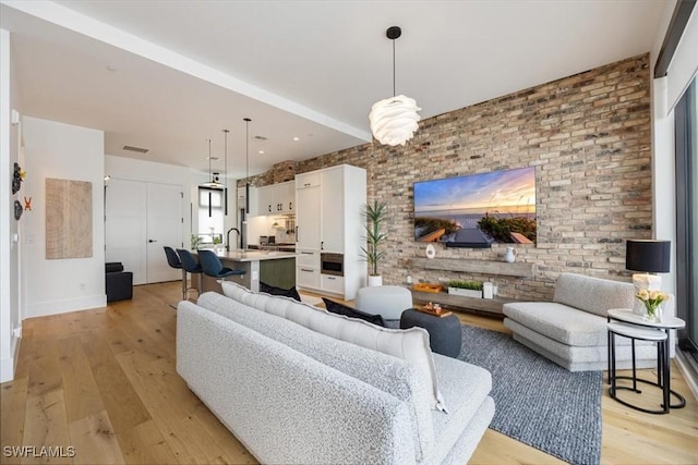 living room featuring sink, light hardwood / wood-style floors, and brick wall