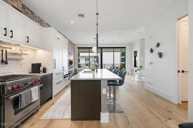 kitchen featuring a kitchen bar, white cabinetry, an island with sink, and designer stove