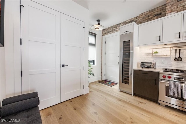 kitchen featuring backsplash, white cabinets, wine cooler, light hardwood / wood-style flooring, and premium stove