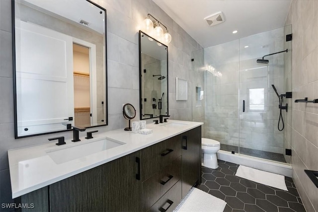 bathroom with vanity, a shower with door, tile patterned flooring, toilet, and tile walls