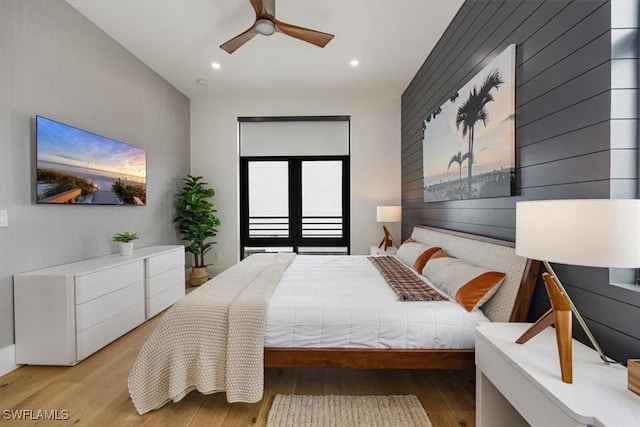 bedroom featuring ceiling fan, wood walls, and light wood-type flooring