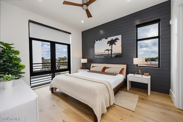 bedroom with light hardwood / wood-style floors, ceiling fan, and wood walls