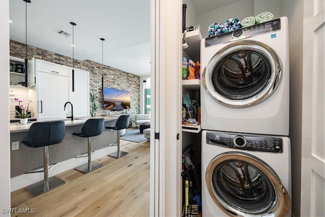 laundry area featuring stacked washer / dryer, light hardwood / wood-style flooring, and brick wall