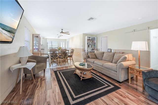 living room with ceiling fan, wood-type flooring, and wood walls