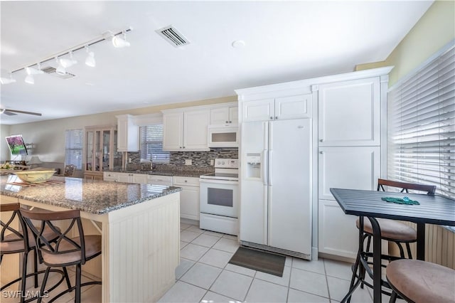 kitchen with a breakfast bar, white appliances, dark stone counters, white cabinets, and light tile patterned flooring