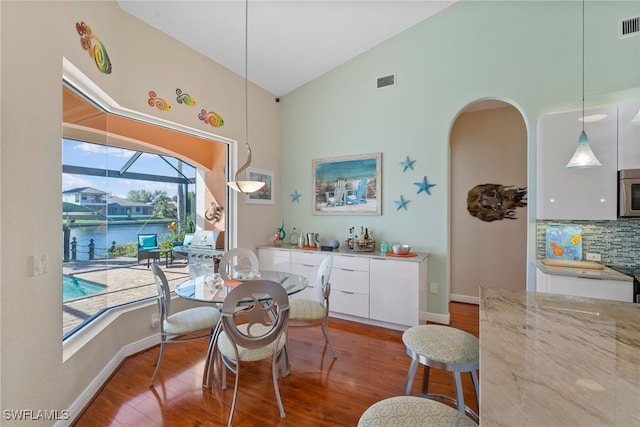 dining room featuring a water view, vaulted ceiling, hardwood / wood-style flooring, and plenty of natural light