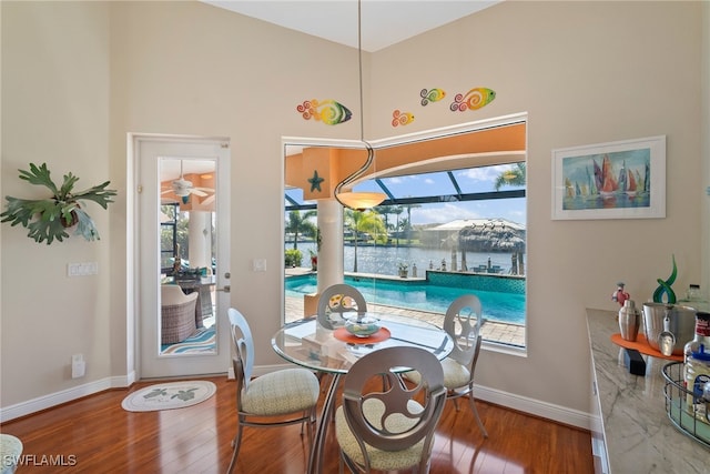 dining space featuring a healthy amount of sunlight, a water view, wood-type flooring, and a high ceiling