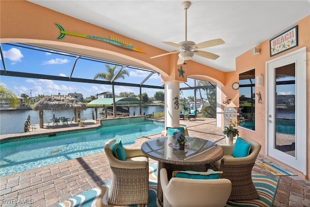 view of swimming pool featuring ceiling fan, a water view, a patio, and glass enclosure