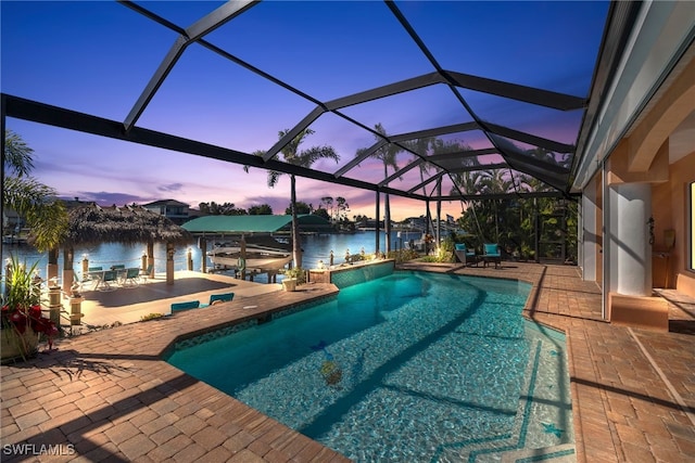 pool at dusk featuring a lanai, a water view, and a patio