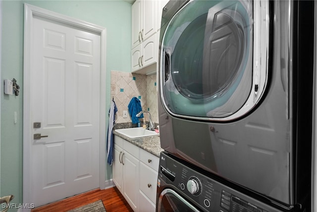 laundry area with cabinets, hardwood / wood-style flooring, stacked washer and clothes dryer, and sink