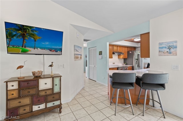 kitchen featuring lofted ceiling, a breakfast bar, light tile patterned floors, and stainless steel refrigerator with ice dispenser