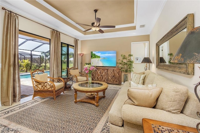 living room with a tray ceiling, ceiling fan, and crown molding