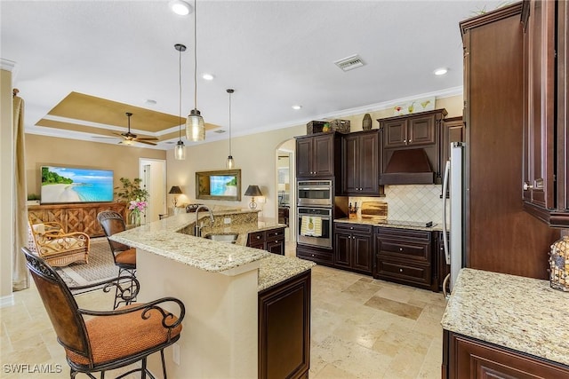 kitchen with custom exhaust hood, a raised ceiling, sink, a large island with sink, and hanging light fixtures