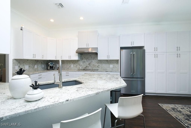 kitchen with light stone countertops, tasteful backsplash, stainless steel fridge, black electric cooktop, and white cabinets