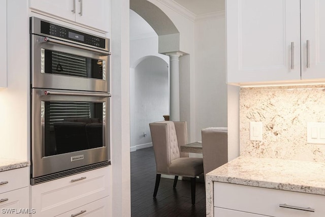 kitchen with white cabinets, stainless steel double oven, ornamental molding, and tasteful backsplash