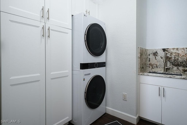 clothes washing area with stacked washer / drying machine, cabinets, and sink