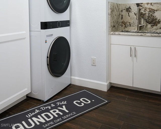 clothes washing area featuring cabinets, stacked washing maching and dryer, and sink