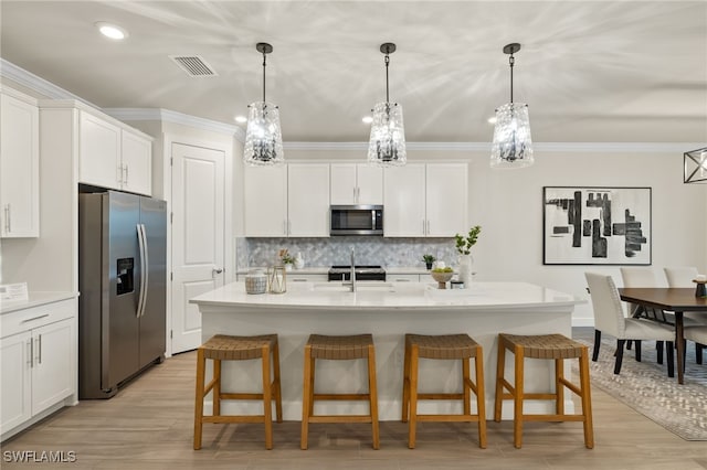 kitchen with appliances with stainless steel finishes, decorative light fixtures, white cabinetry, and an island with sink